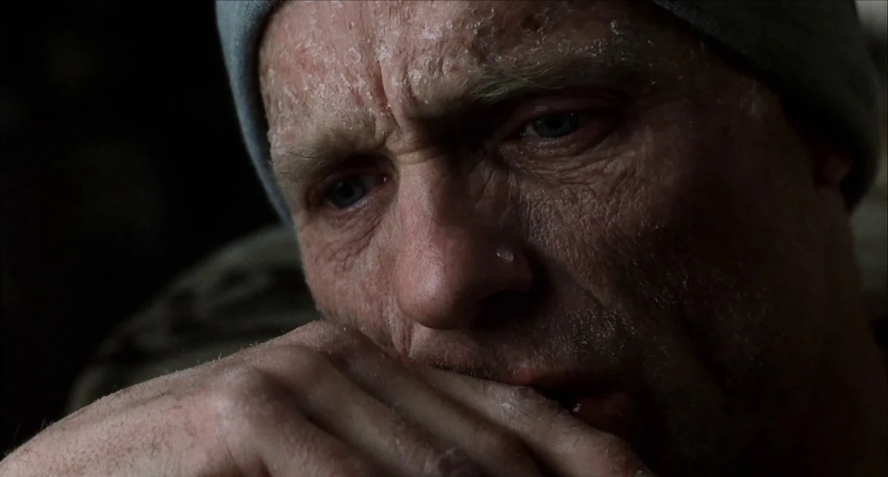 The Hours (2002) movie still: closeup — A dark, dimly lit environment surrounds a man with weathered, flaky, textured skin. He rests his face on his…