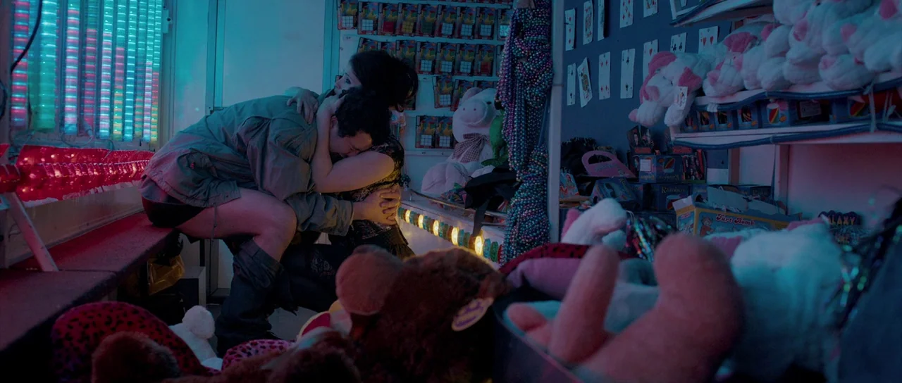 Byzantium (2012) movie still: medium — A carnival game booth is filled with rows of plush toys and playing cards. A young couple hugs inside the…