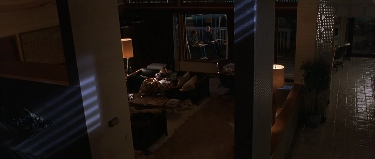 Bandits (2001) movie still: wide — A split-level living area features a sofa in the center with modern lamps. Two people sit together on the sofa…