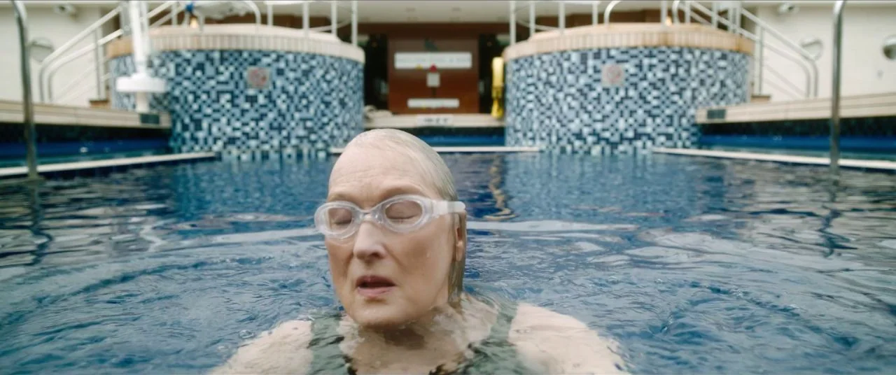 Let Them All Talk movie still: medium — An outdoor swimming pool features blue mosaic tile walls and a metal railing. A woman wearing goggles and a…
