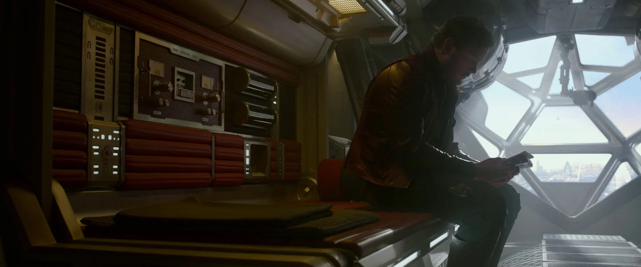 Guardians of the Galaxy (2014) movie still: medium — A spaceship cabin featuring geometric windows and red upholstered bench seating. A man sits…
