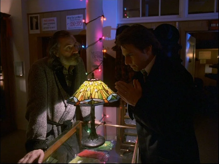 Eyes Wide Shut (1999) movie still: medium — A dimly lit shop interior with wood-paneled walls and Christmas lights wrapped around a pillar. A…