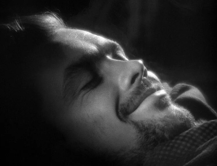 Prison (1949) movie still: closeup — A man's face is illuminated in profile against a dark background. He lies down with his eyes closed and a faint…