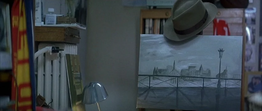 The Truth About Charlie (2002) movie still: medium — A cluttered indoor workspace features a small canvas propped on a wooden easel frame. A gray…