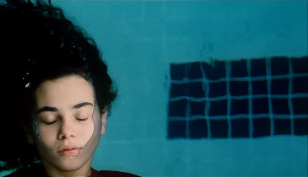 Nenette et Boni (1996) movie still: closeup — A person floats underwater in a pool with teal tiled walls. The subject keeps their eyes closed as…