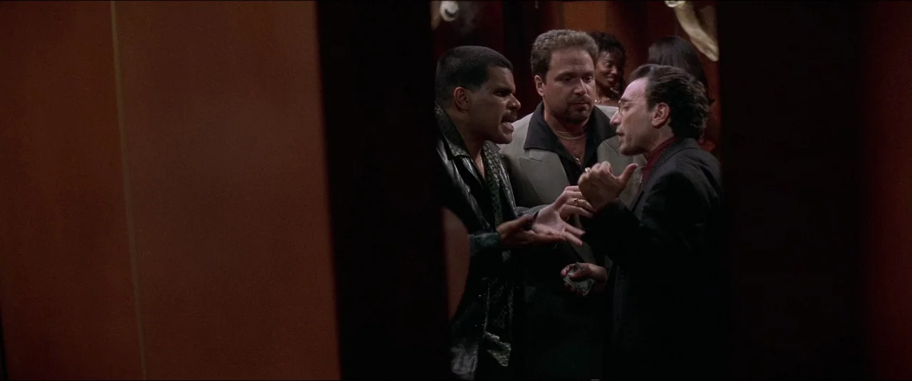 Snake Eyes (1998) movie still: medium — A dimly lit club interior with dark wood paneled walls and crowded background space. Three men in…
