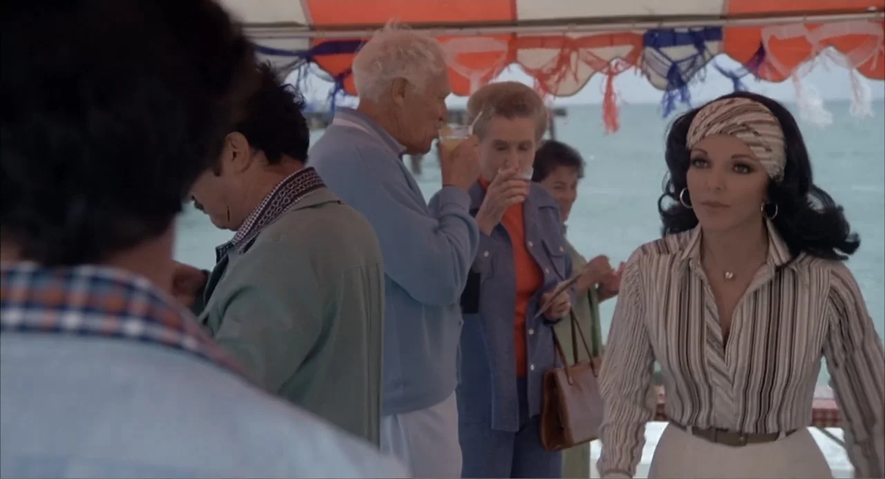 Empire of the Ants (1977) movie still: medium — A group of people stands under a striped canopy on a pier near water. A woman in a striped shirt…