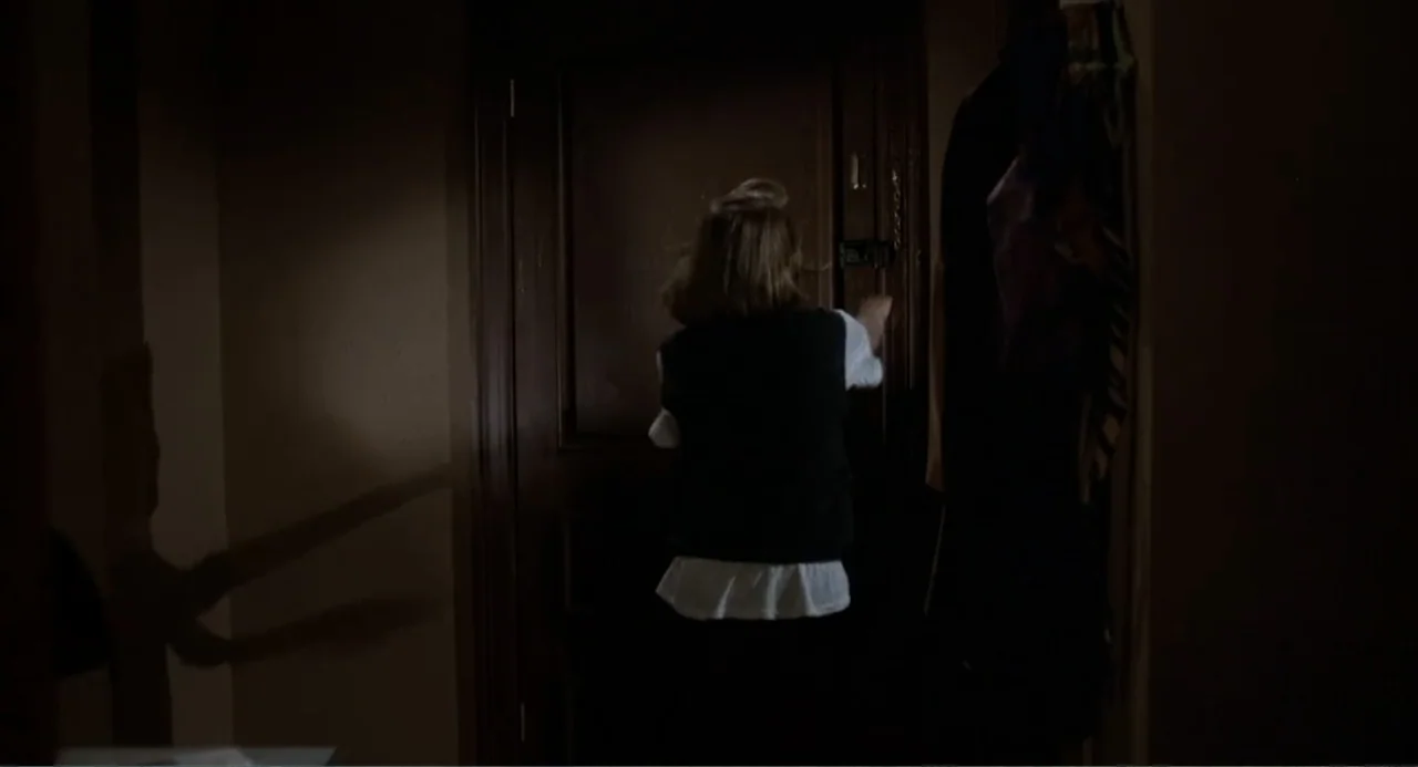 I, Madman (1989) movie still: medium — A dimly lit residential apartment entrance features a dark wooden door and hanging coats. A young girl in a…