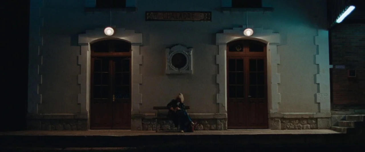 Knife+Heart (2018) movie still: wide — A stone-walled train station building with two wooden doors features a nameplate reading CHALADRE. A person…