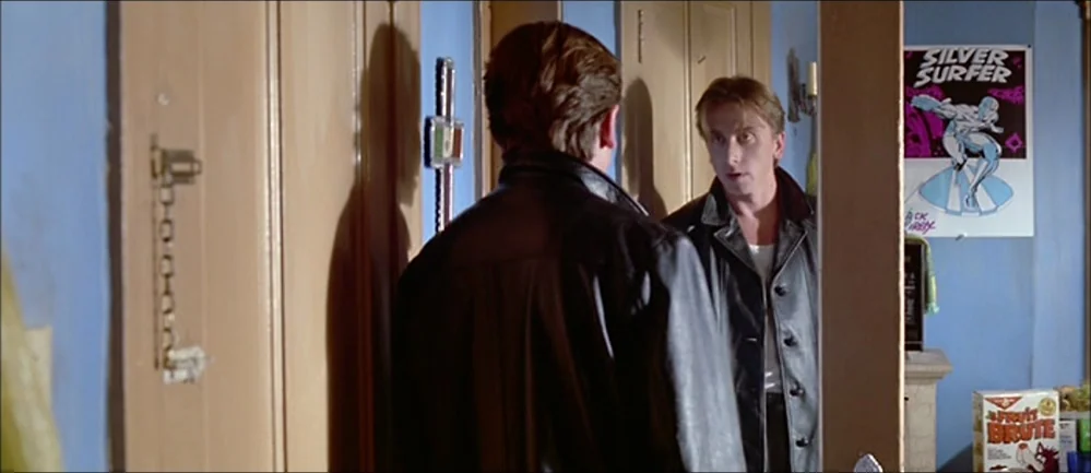 Reservoir Dogs (1992) movie still: medium — A room with light blue walls and wood paneling has a mirror on the wall. A man stands facing his own…