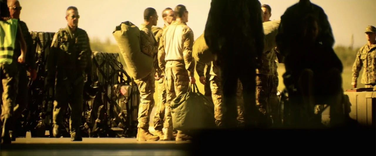 Bloodshot (2020) movie still: fullbody — A group of soldiers in camouflage uniforms walk across an outdoor tarmac area. The men carry large…