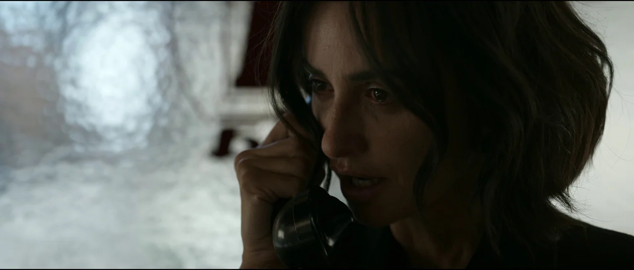 Ferrari (2023) movie still: closeup — A dark indoor setting featuring a textured glass partition behind the subject. A woman holds a vintage black…