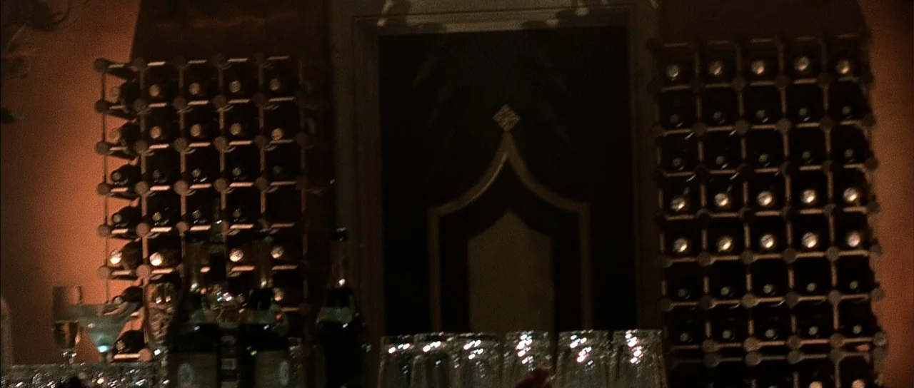A Man Apart (2003) movie still: establishing — A dimly lit bar features dark wood shelving units filled with stacked wine bottles. Rows of clear…