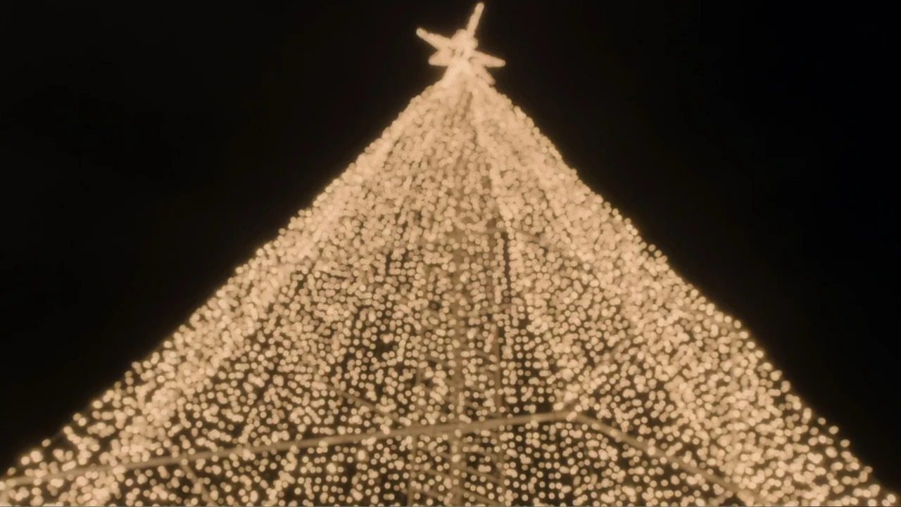 Peppermint and Postcards (2023) movie still: wide — A tall conical structure is covered in dense warm fairy lights. A star-shaped ornament sits at…