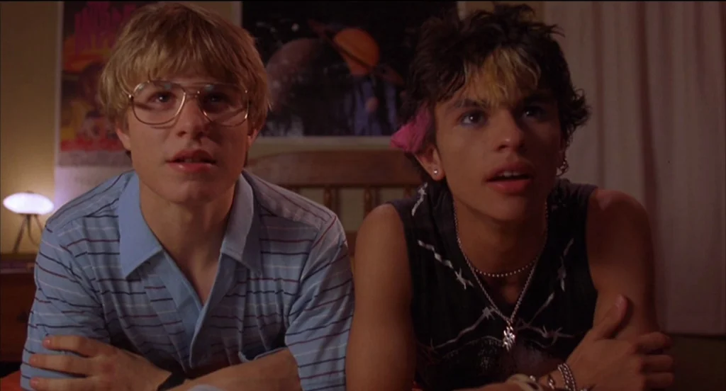 Mysterious Skin (2004) movie still: medium — A dimly lit bedroom features walls decorated with posters including a planet image. Two young men sit…
