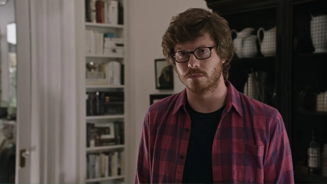 The Intern (2015) movie still: medium — A residential living room features white built-in bookshelves stocked with various items. A man with brown…