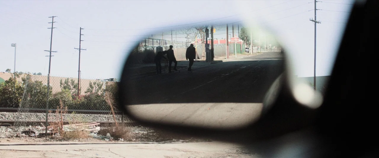Destroyer (2018) movie still: wide — An urban industrial area is viewed through the car's side mirror. Three figures walk away from the viewer along…