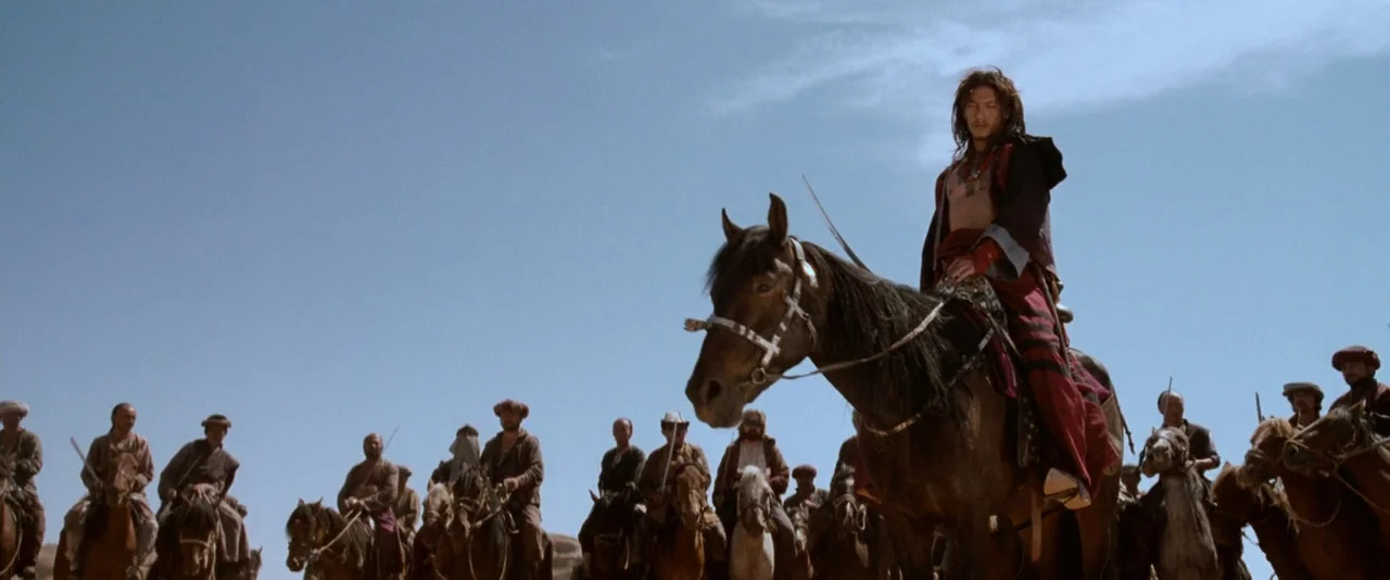 Crouching Tiger, Hidden Dragon (2000) movie still: wide — A vast, sun-drenched desert plain under a clear blue sky. A group of men on horseback wait…