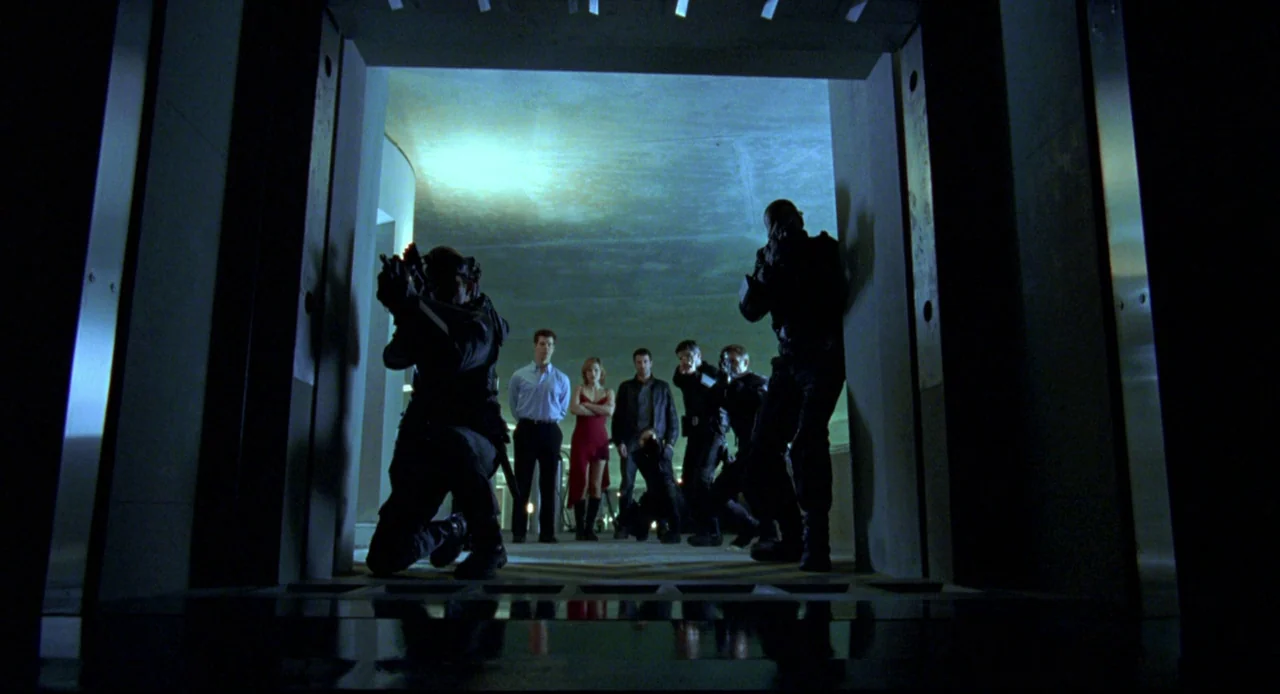 Resident Evil (2002) movie still: wide — A dark concrete portal frames a group of tactical operatives in an illuminated garage. The armed team…