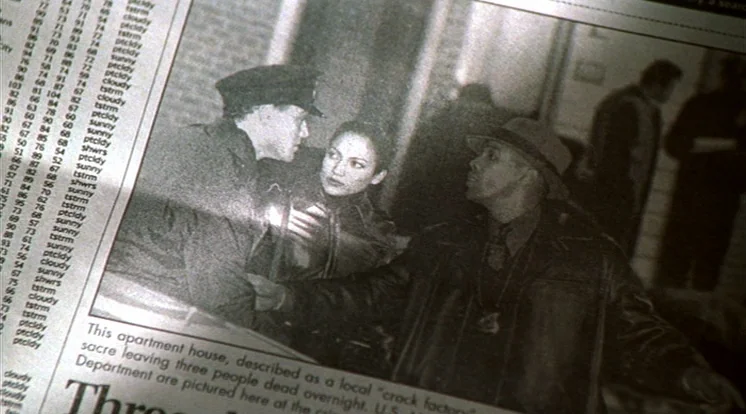 Out Of Sight (1998) movie still: closeup — A close-up photograph printed in a newspaper shows three people in dark clothing. An officer in a cap…