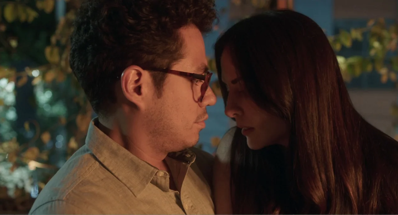 Casando a mi Ex (2023) movie still: medium — A man and a woman stand close together in an outdoor area at night. The pair look directly at each…