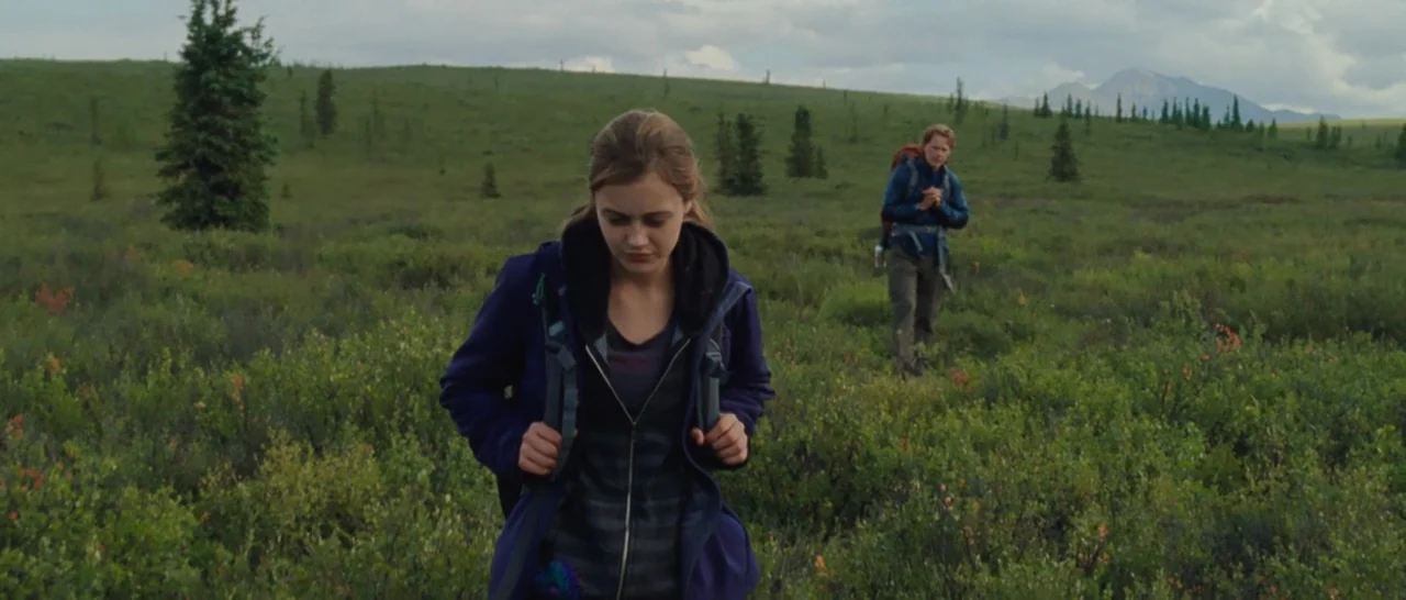 Wildlike (2014) movie still: medium — A vast, open subarctic landscape features low-lying green shrubs and sparse evergreen trees. A young woman…