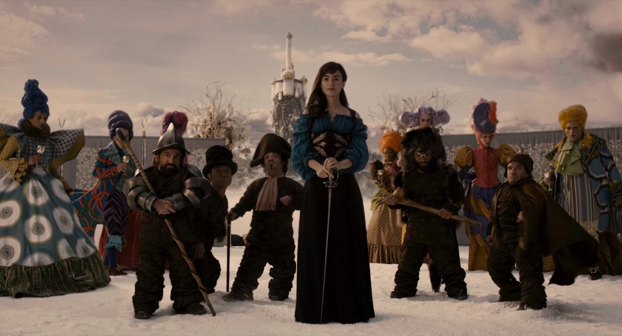 Mirror Mirror (2012) movie still: fullbody — A group of diverse figures stand on a wide, snowy plain under a cloudy sky. A woman holds a sword,…
