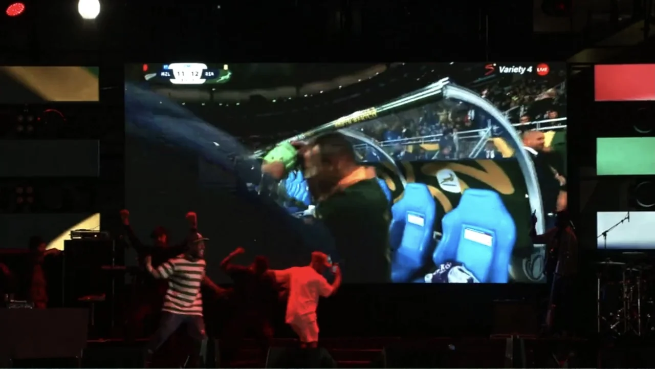 African Throne World Tour (2024) movie still: medium — An outdoor stage features a massive video display showing a live sports event broadcast.…