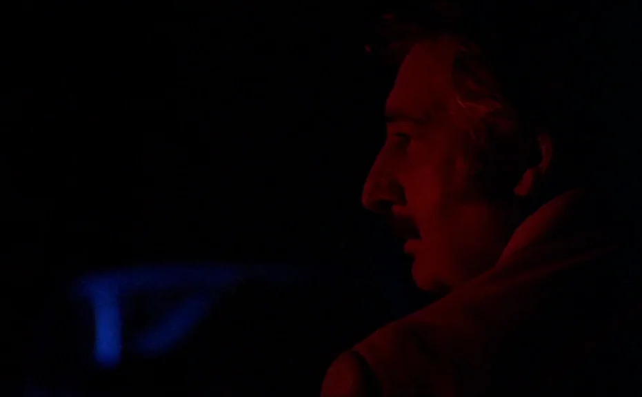 Diva (1981) movie still: closeup — A dark vehicle interior features a man lit by flickering colored exterior lights. The subject stares out of the…