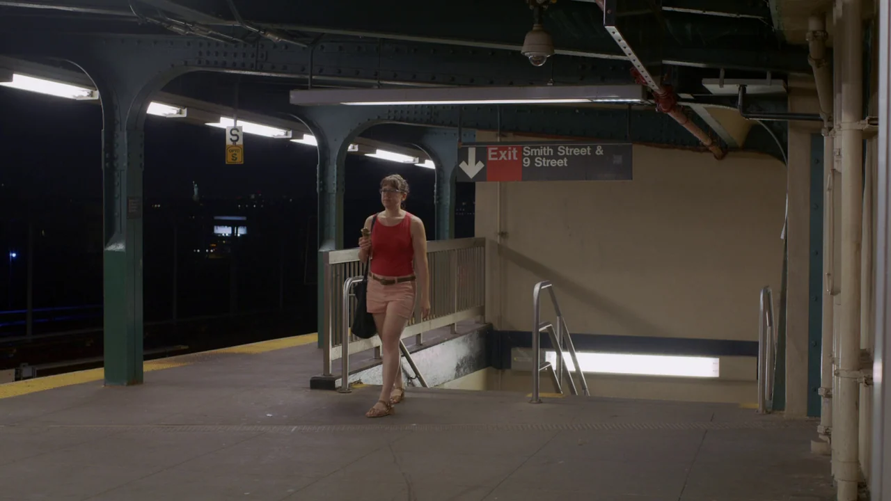The Feeling That the Time for Doing Something Has Passed (2023) movie still: fullbody — A night view of an open-air subway platform with metal…