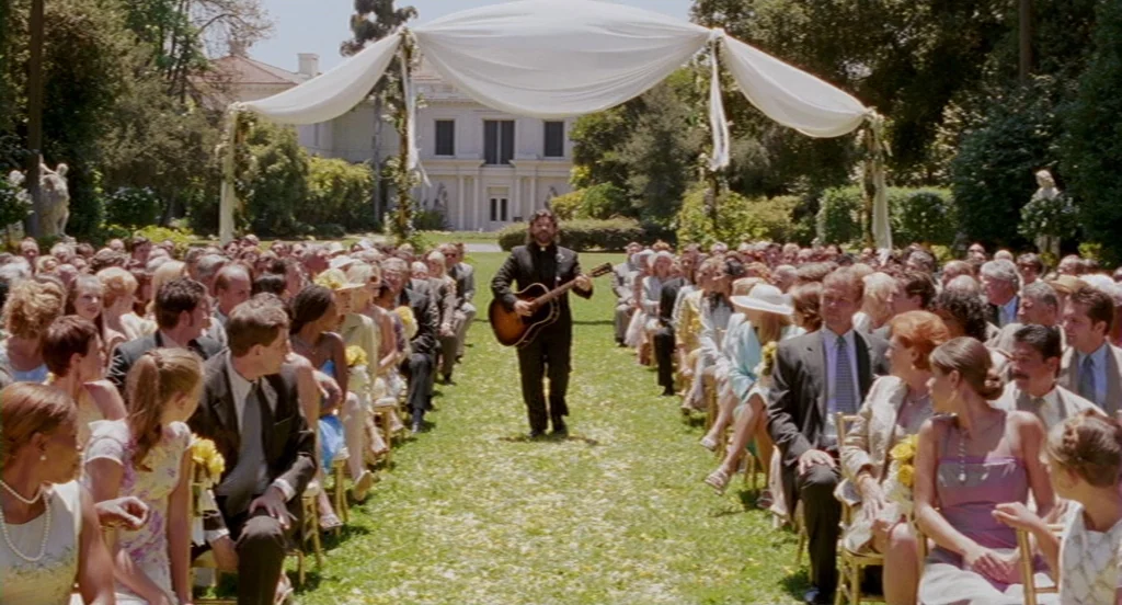 Intolerable Cruelty (2003) movie still: wide — A formal wedding ceremony takes place on a lawn between rows of seated guests. A man in a dark suit…