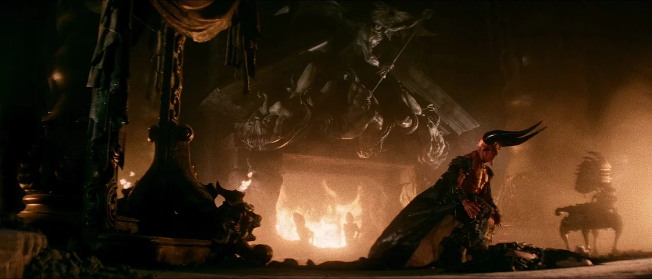 Legend (1985) movie still: wide — A dark subterranean space features a massive stone fireplace carved with grotesque, demonic figures. A horned…