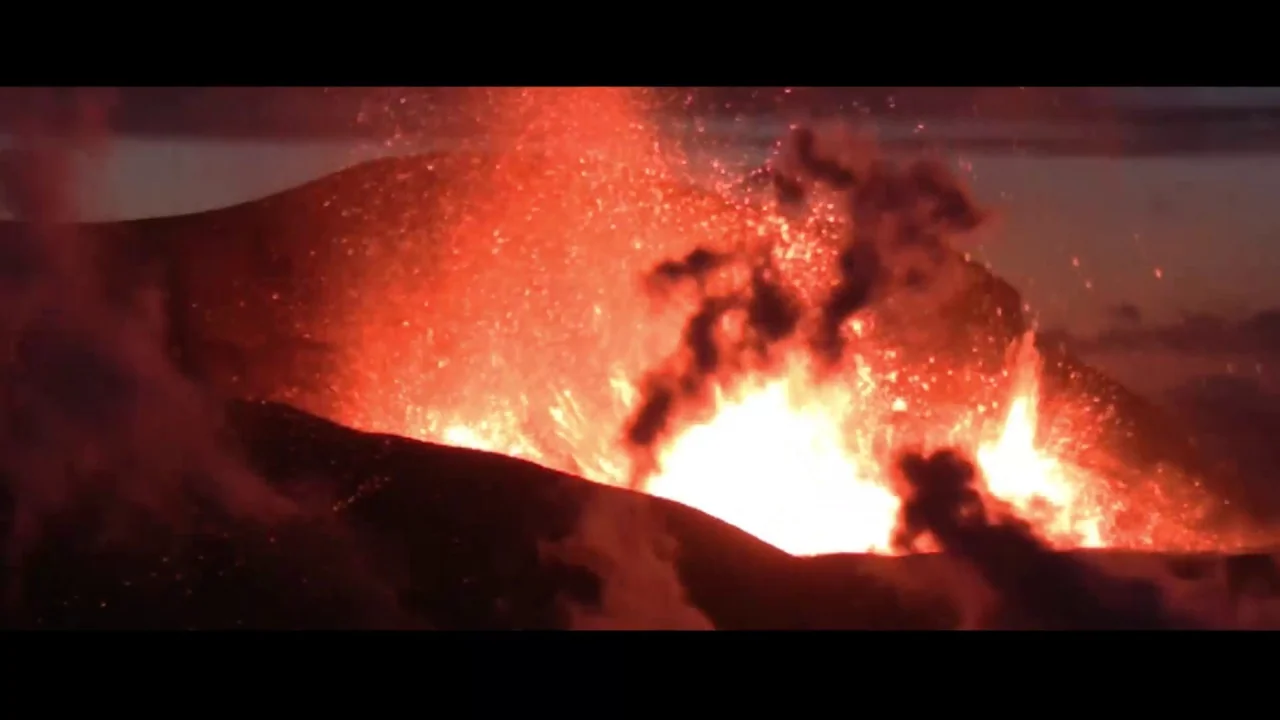Collective: Unconscious (2016) movie still: establishing — A dark mountainous landscape with active volcanic eruption pouring bright lava across the…