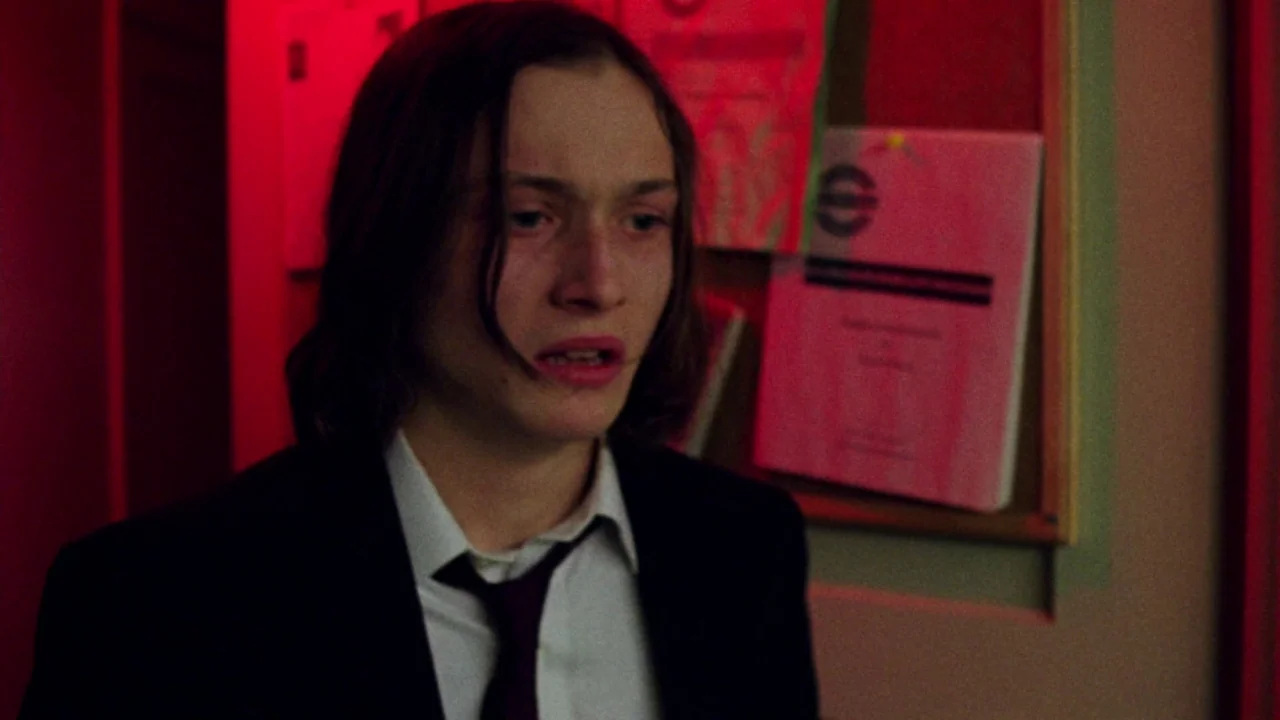 I Am Not a Serial Killer (2016) movie still: medium — An interior hallway lit by vibrant red light contains a bulletin board with papers. A teenage…