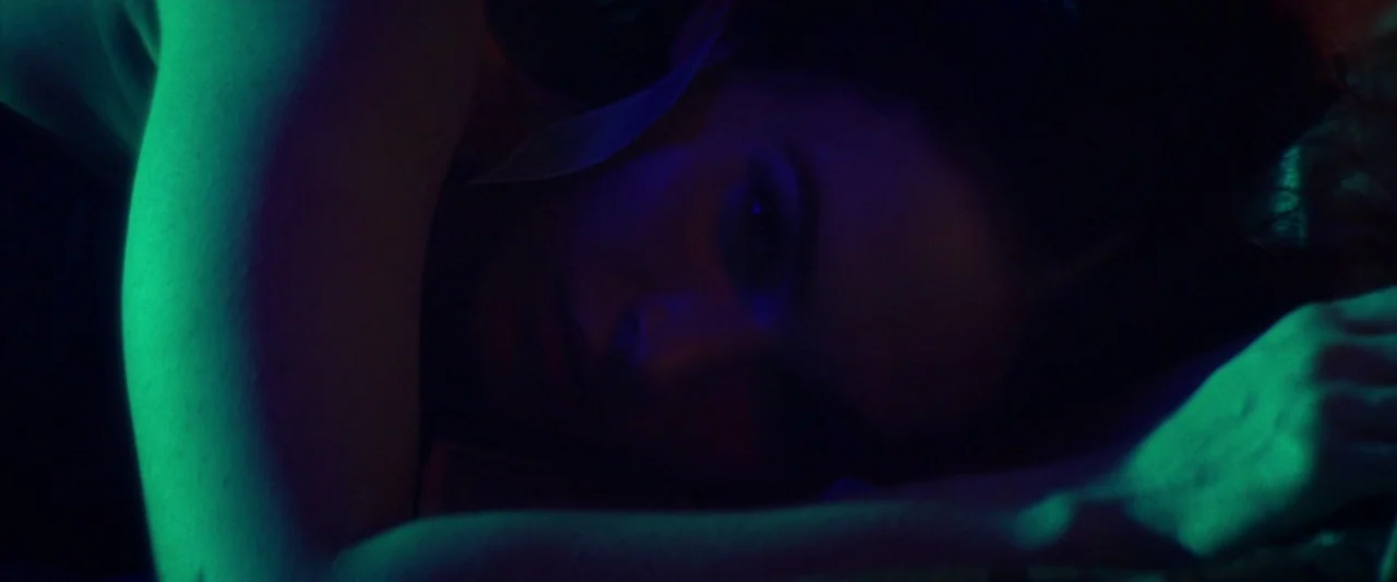 Zeroville (2019) movie still: closeup — A dimly lit room is illuminated by a sharp green light source from one side. A young woman lies with her…