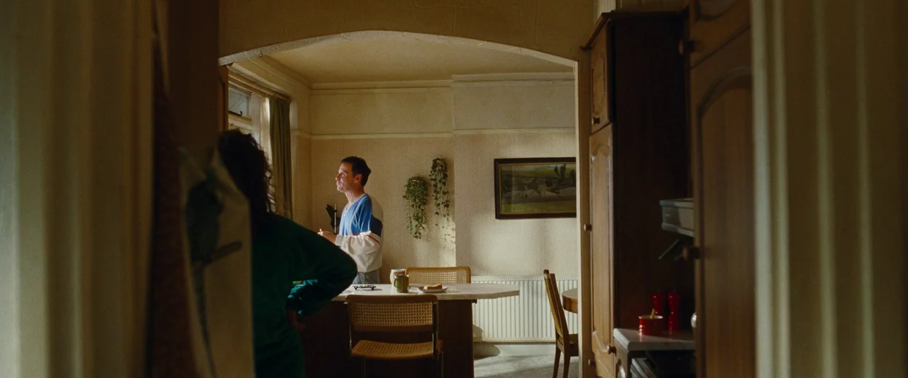 All Of Us Strangers (2023) movie still: wide — A domestic dining area featuring textured wallpaper, wooden furniture, and framed artwork on walls. A…