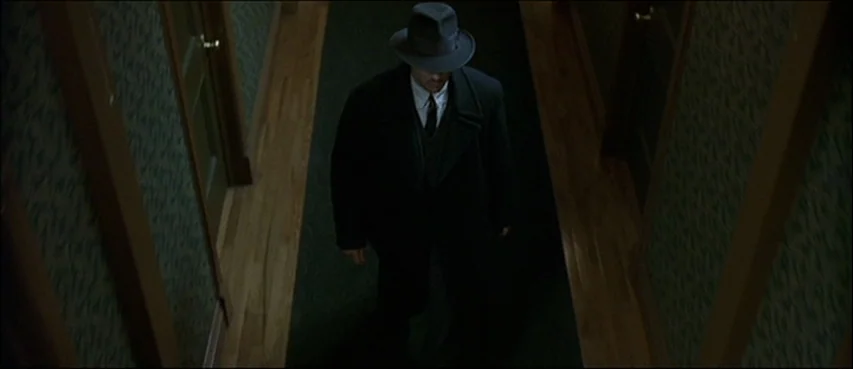 Road To Perdition (2002) movie still: fullbody — A narrow residential hallway with green patterned wallpaper and dark wooden door frames. A man…