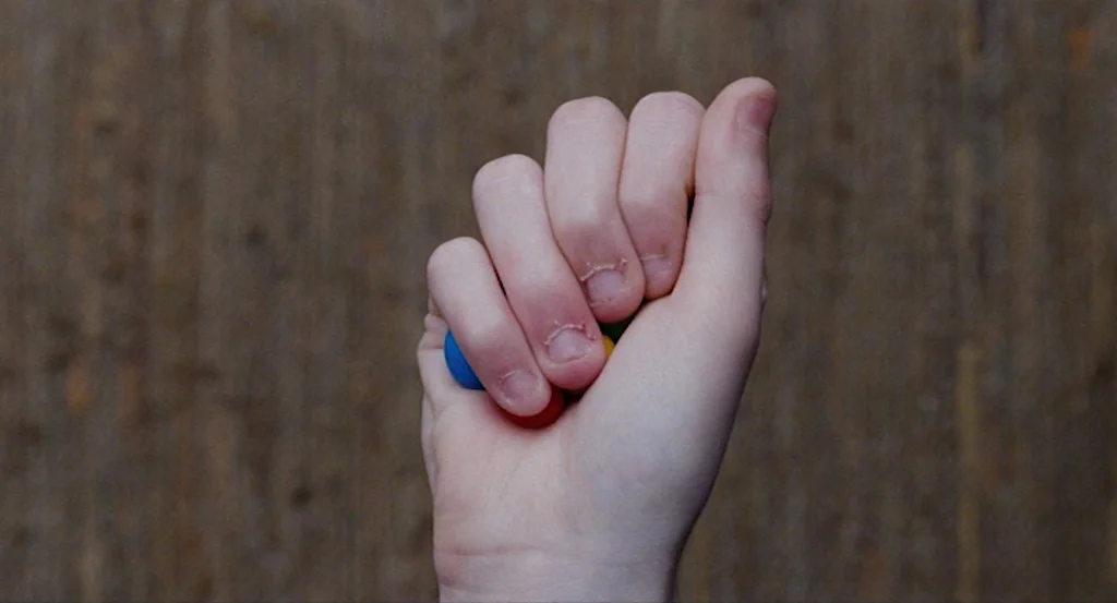 Louder Than Bombs (2015) movie still: closeup — A close-up view of a human hand held in a fist against a textured surface. The fingers are curled…
