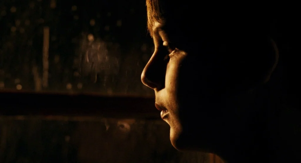 Mimic (1997) movie still: closeup — A dark space at night with a person standing by a glass surface. The subject is seen in side profile against the…