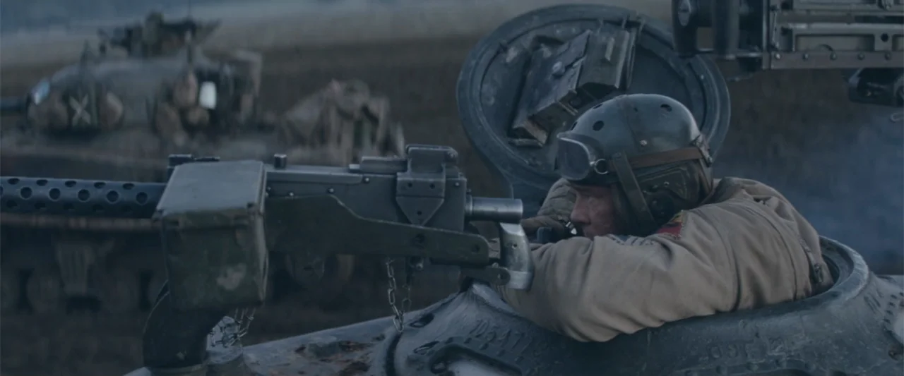 Fury (2014) movie still: medium — A muddy, desolate battlefield contains multiple military tanks positioned in a line. A male tank commander peers…