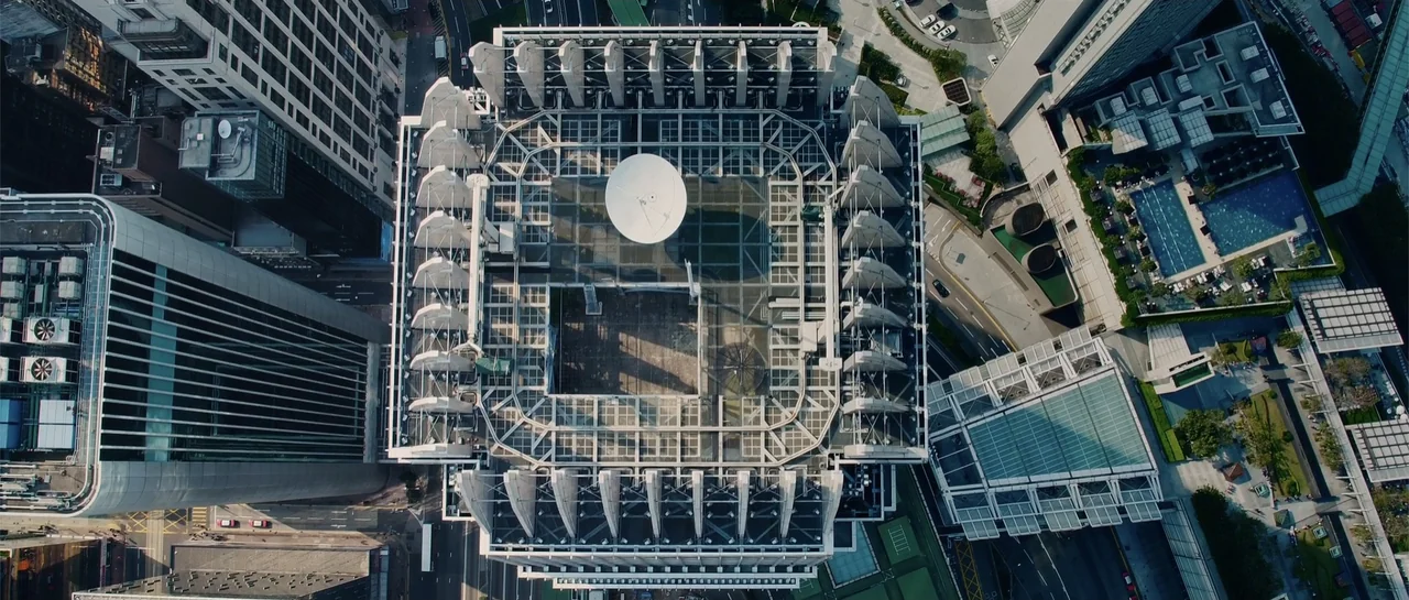 Line Walker (2016) movie still: establishing — A high-angle top-down view shows the industrial roof of a modern city skyscraper. The roof features a…