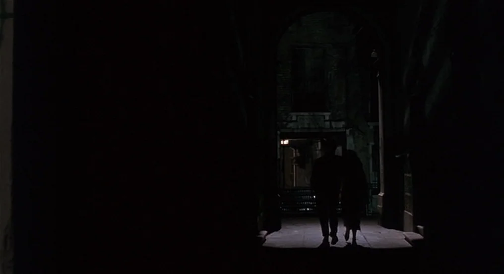 The Comfort of Strangers (1990) movie still: wide — A stone masonry archway transitions into a narrow passage at night. A couple walks away from the…