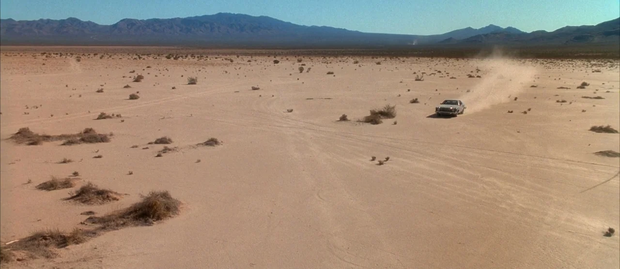 Casino (1995) movie still: establishing — A vast, flat desert basin features sparse low-lying scrub brush and distant mountain ranges. A single…