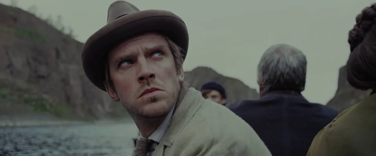 Apostle (2018) movie still: medium — Several people travel in a small vessel through a waterway flanked by high cliffs. A man wearing a hat looks…