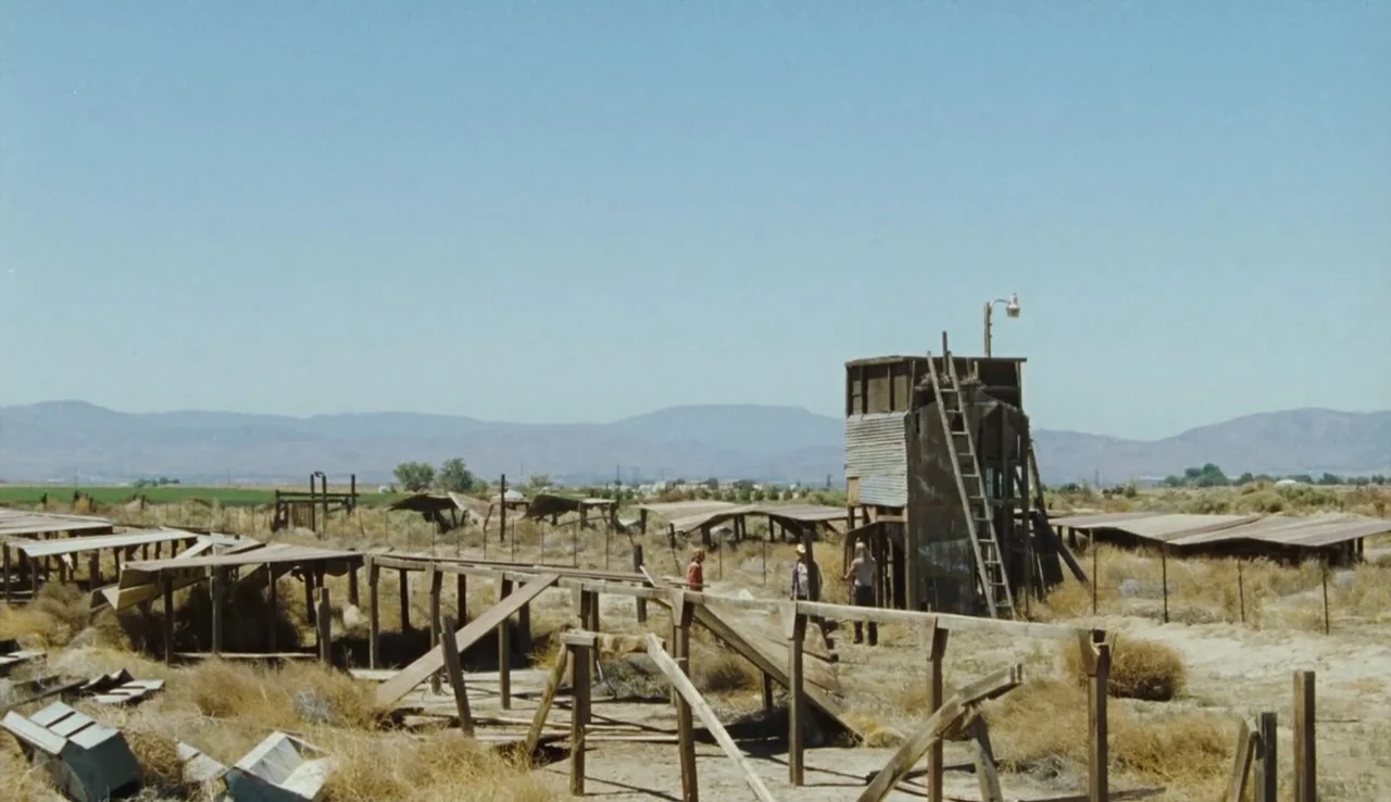 The Devil’s Rejects (2005) movie still: wide — A dry, desolate field features weathered wooden platforms and a central rusted observation tower.…