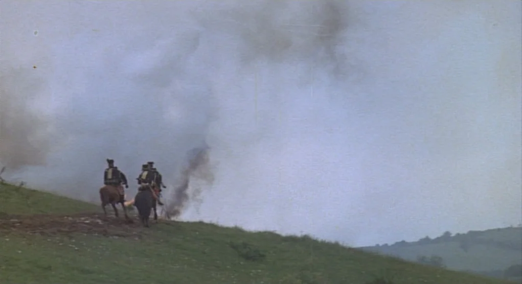 Time Bandits (1981) movie still: wide — A grassy hill ridge is obscured by thick white plumes of battle smoke. Two soldiers on horseback ride away…