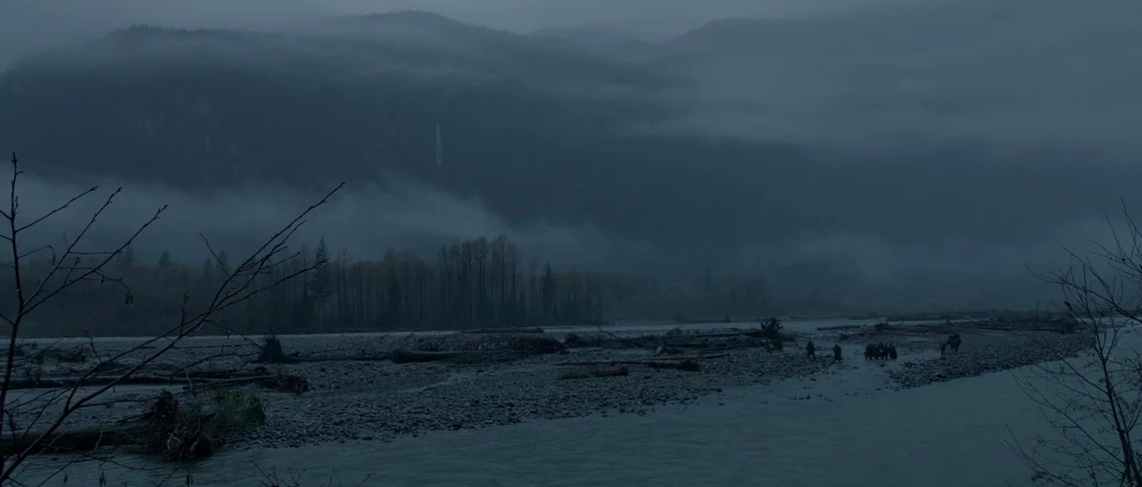 The Revenant (2015) movie still: wide — A wide, foggy mountain valley contains a shallow river and extensive rocky riverbed terrain. A small group…