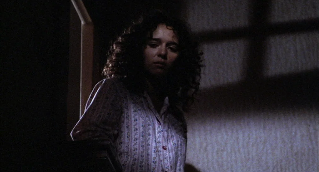The Indian Runner (1991) movie still: medium — A dark, dimly lit staircase features a distinctive cross-shaped shadow cast upon the wall. A young…