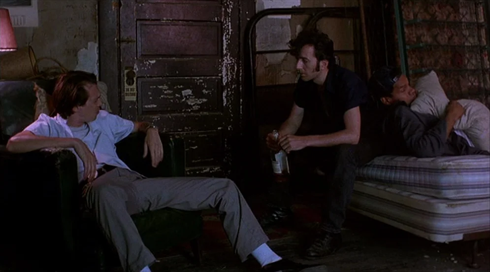 Mystery Train (1989) movie still: medium — A sparsely furnished room features a distressed wooden door and a mattress on the floor. Three men…