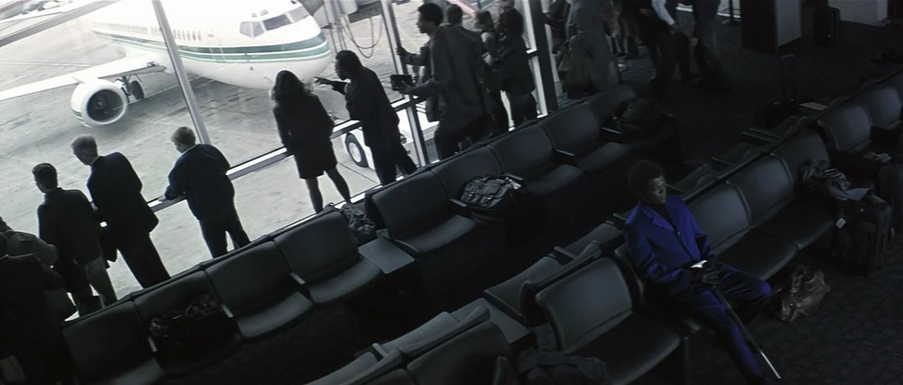 Unbreakable (2000) movie still: wide — A spacious, quiet airport terminal terminal features rows of empty chairs facing large glass windows. A man…